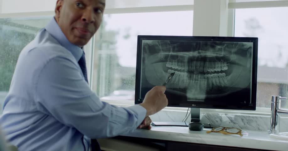 A dentist shows a patient an xray on a monitor in an office