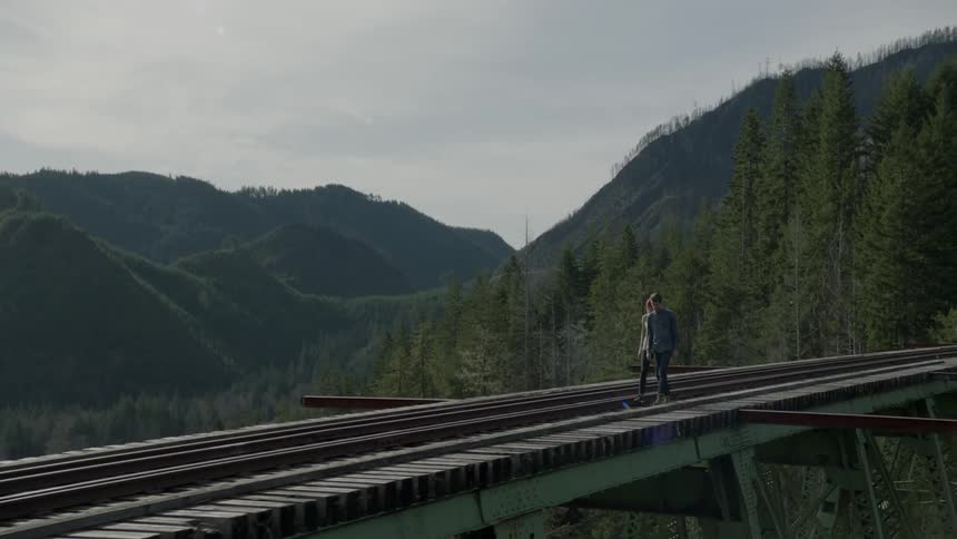 Two people are walking across a bridge with a train track