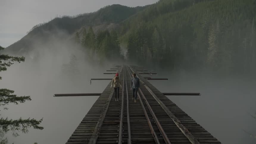 Two people cross a train bridge in the mountains