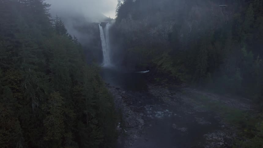 A waterfall is dropping into a stream on a foggy day