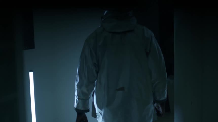 A person wearing a full body hazard suit walks through a building while a light strobes