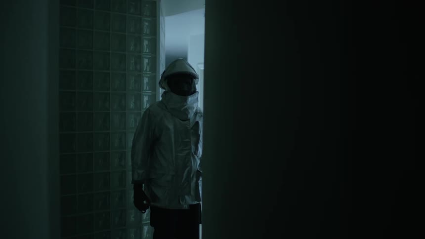 A man stands in a doorway wearing a reflective silver suit as lights flash on and off