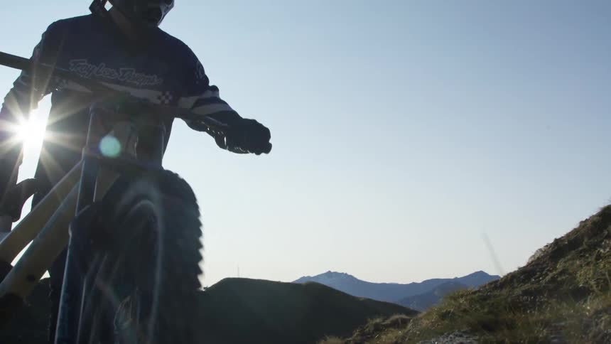 Man pushes bicycle up slope with mountains on horizon