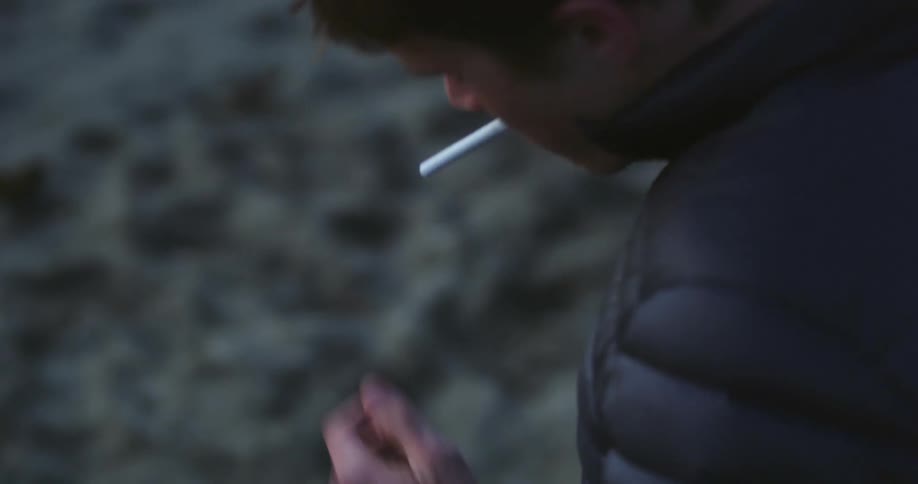 A teenager puts a cigarette in his mouth lights it and smokes