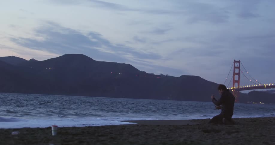 Man kneeling on a beach fails to light a cigarette and gets angry and frustrated