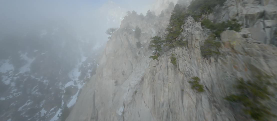 Snow covers a forest at the bottom of a canyon as fog starts to form above