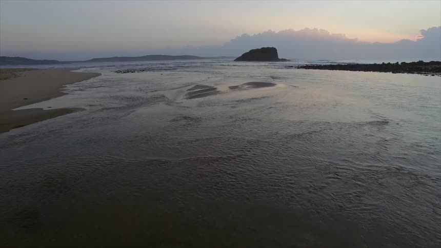 Waves are moving around as the sun sets in the distance