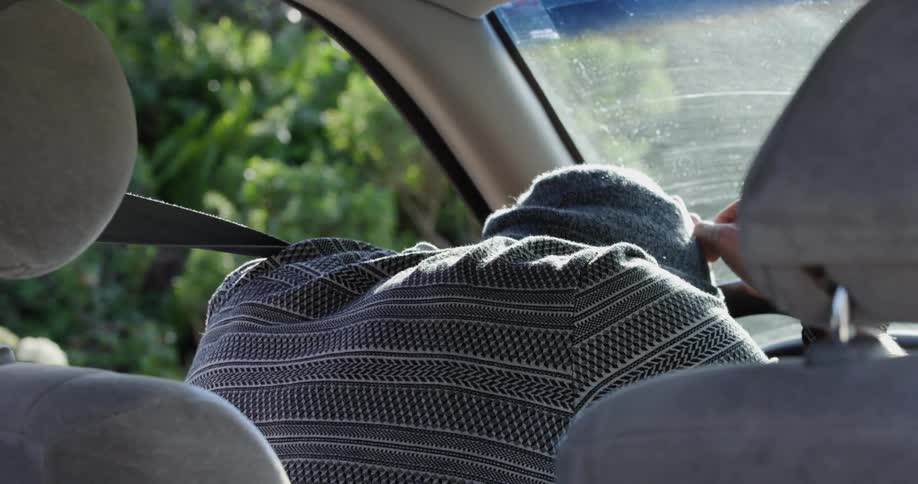 A stressed man crying in the drivers seat of a parked vehicle while leaning against the steering wheel