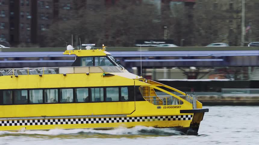 Yellow ferry boat travels across the sea passing by a bridge