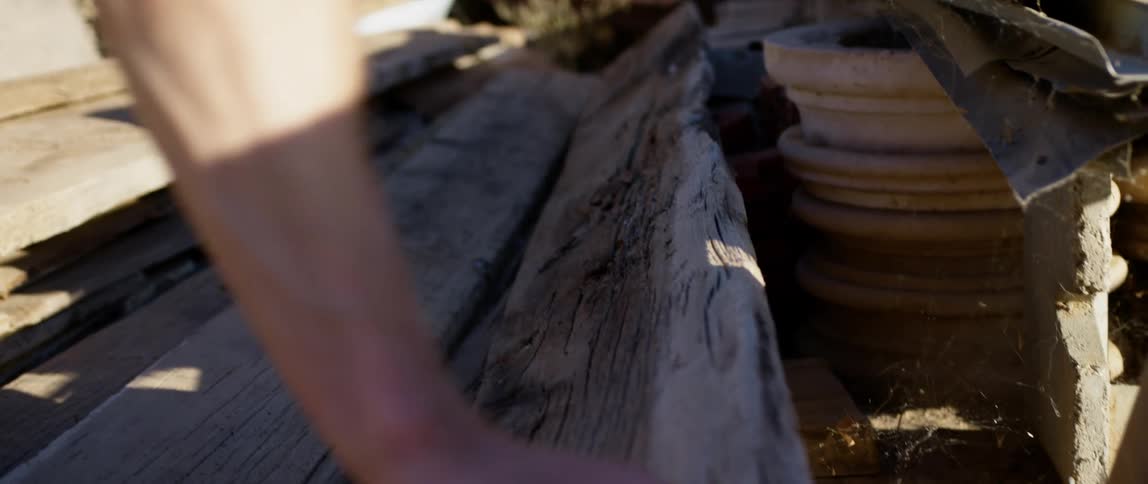 A persons hand moving a plank of wood next to plant pots and cobwebs
