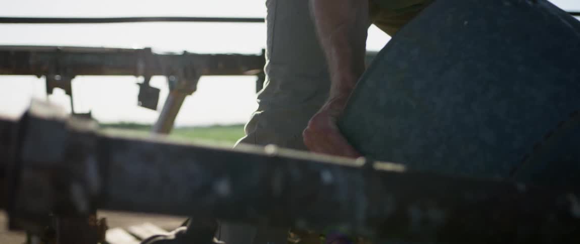 A man struggles to lift a large metal bowl on a ranch