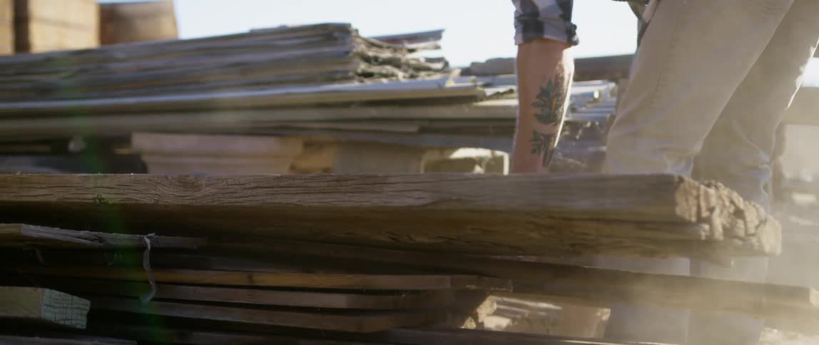 A person picking up and dropping planks of wood with the sky in the background