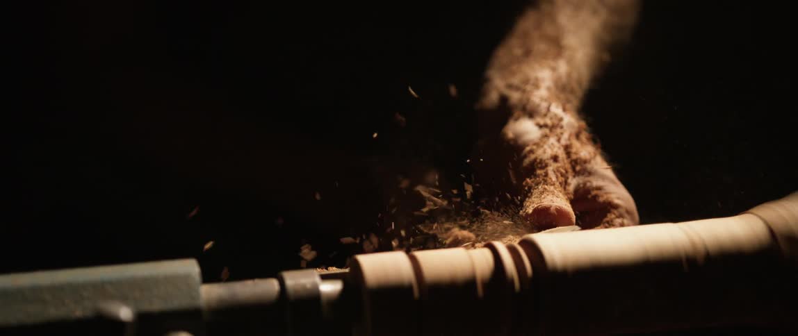 A persons hand shaving wood on a spindle