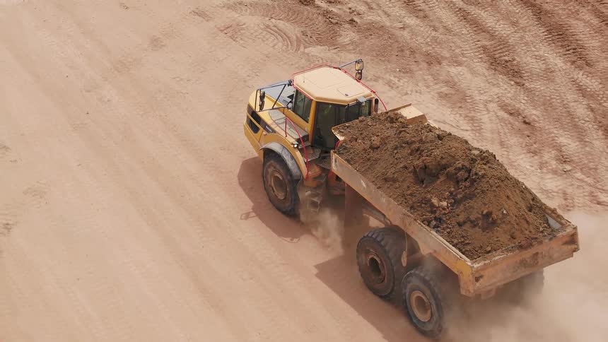A dump truck filled with soil drives down a dirt road