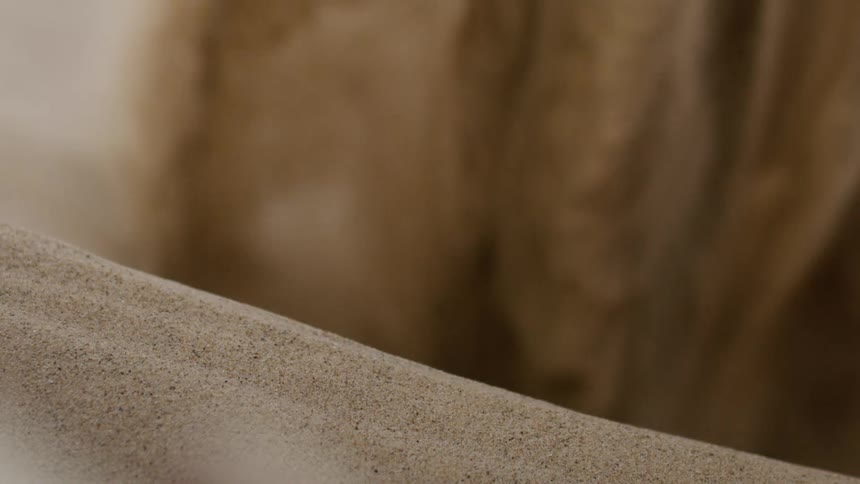 A pile of sand slowly moves as more pours into a hole