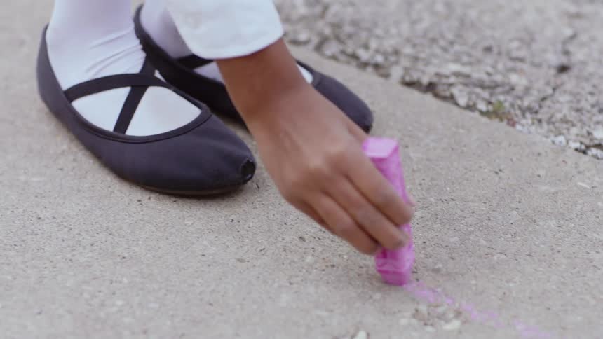 A young girl draws on cement with sidewalk chalk