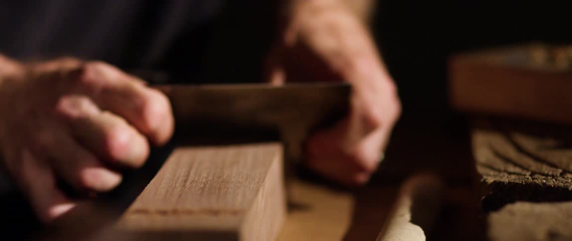 A persons hand shaving wood with a tool