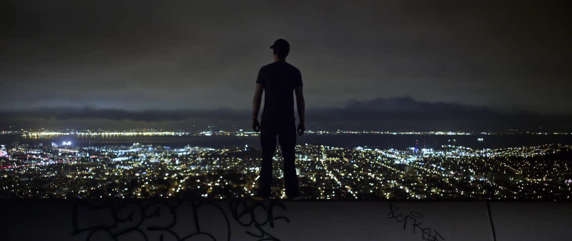 Man with a cap and t shirt is silhouetted against the skyline at night