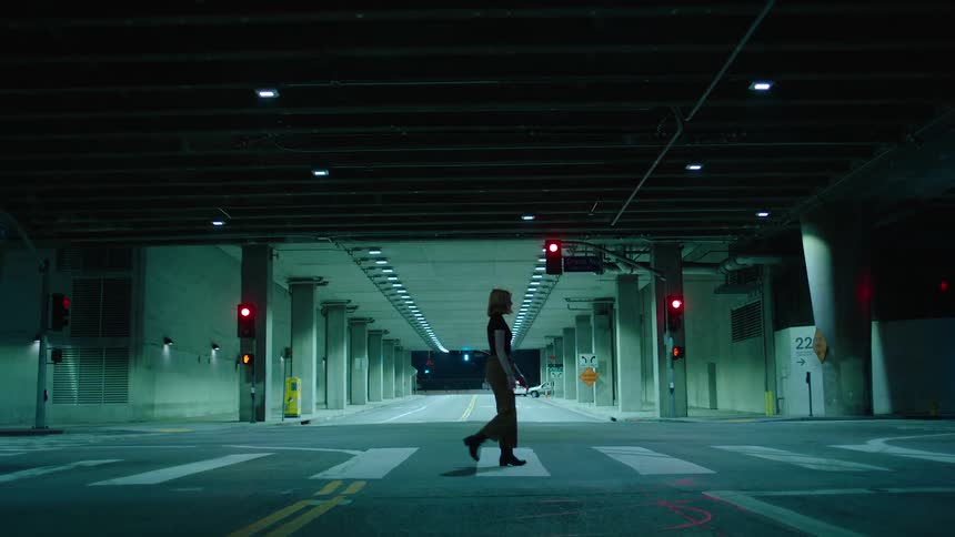 Woman walks on a zebra pass under a structure in the city at night