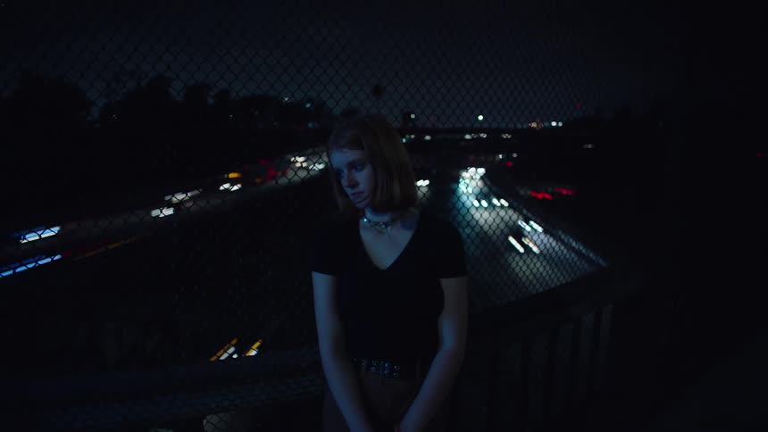 Teen woman standing in overpass over traffic at night