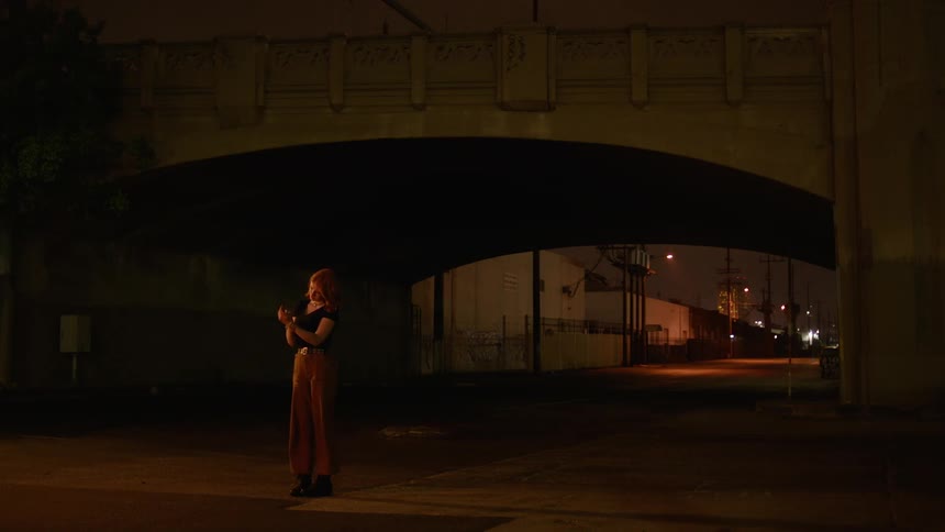 Woman stands near a tunnel at night as she flicks a lighter on and off