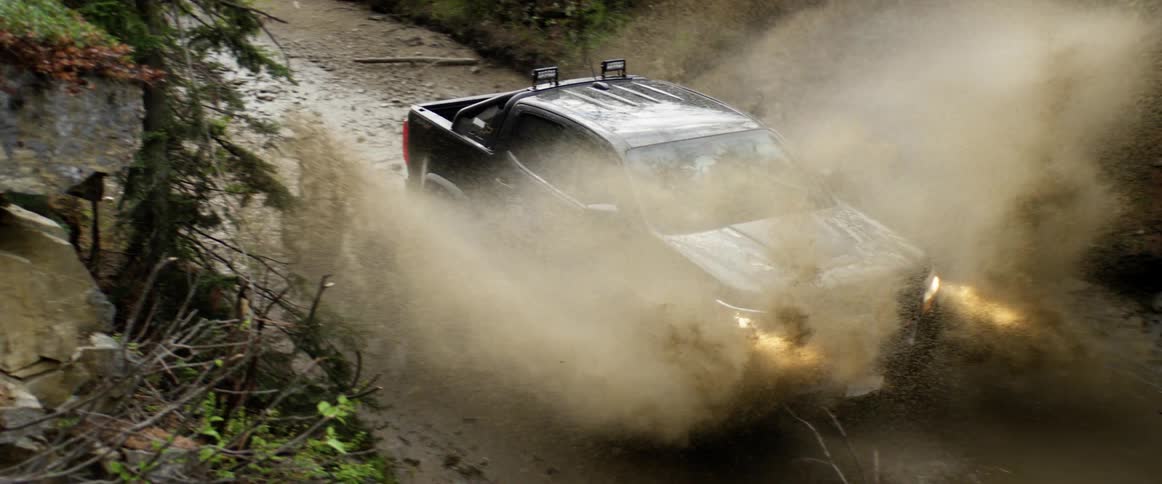 Truck driving off road through a large mud puddle on a dirt road
