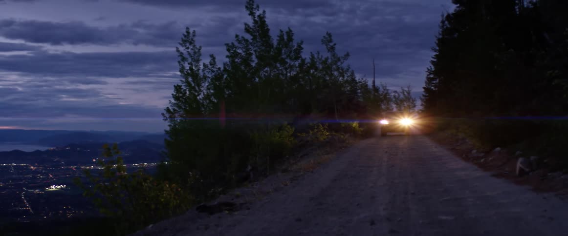 Pickup truck with headlights illuminating the road drives downhill at dusk