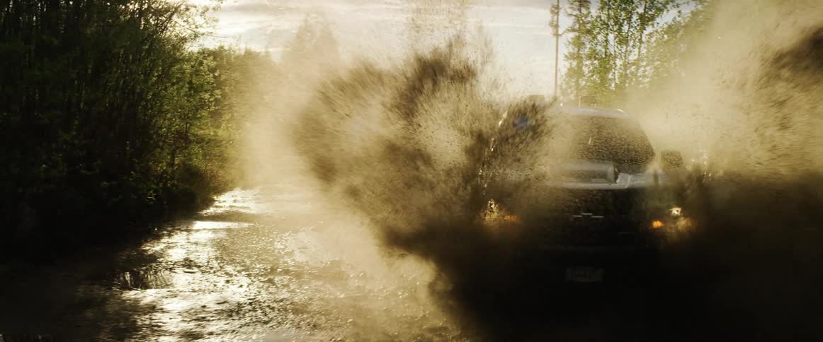 A car drives through a large puddle on a road next to a forest
