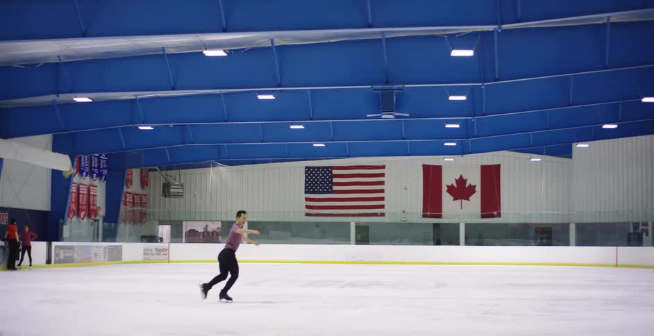 Male figure skater does a spin on the ice in an arena