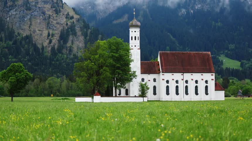 A church sits in a meadow at the base of a mountain