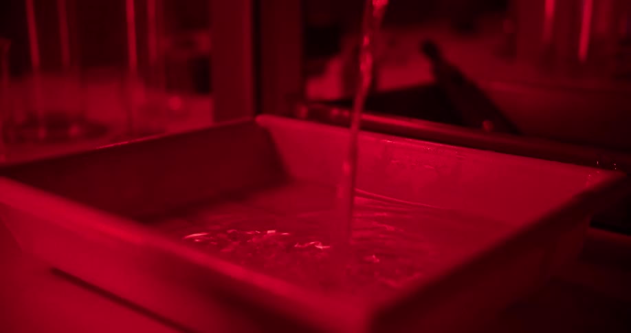 Water pouring into a plastic tray in a dark room illuminated by a red light