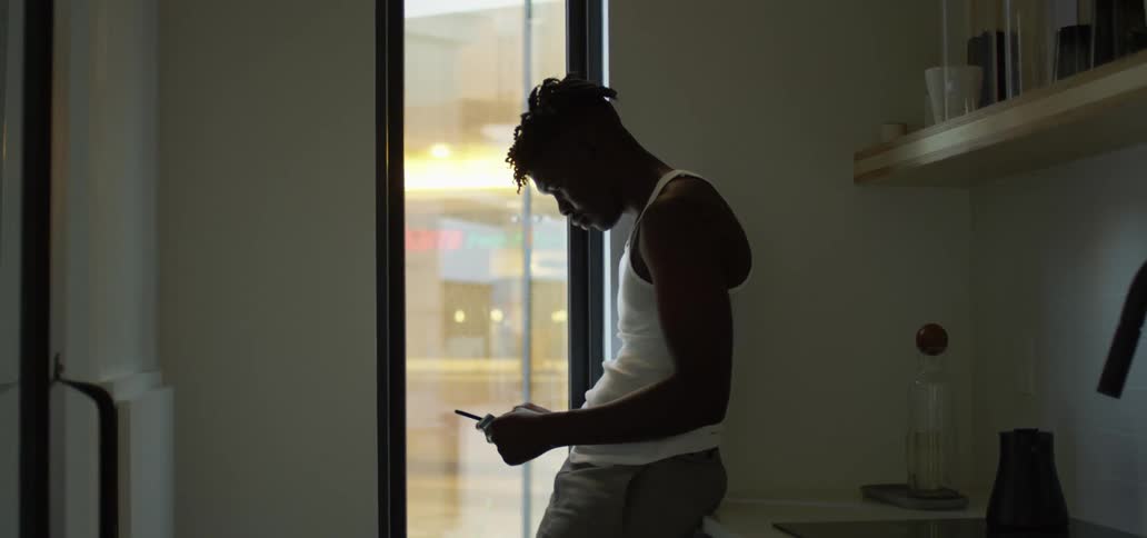 A teenager leans against a counter at home and texts on his cell phone