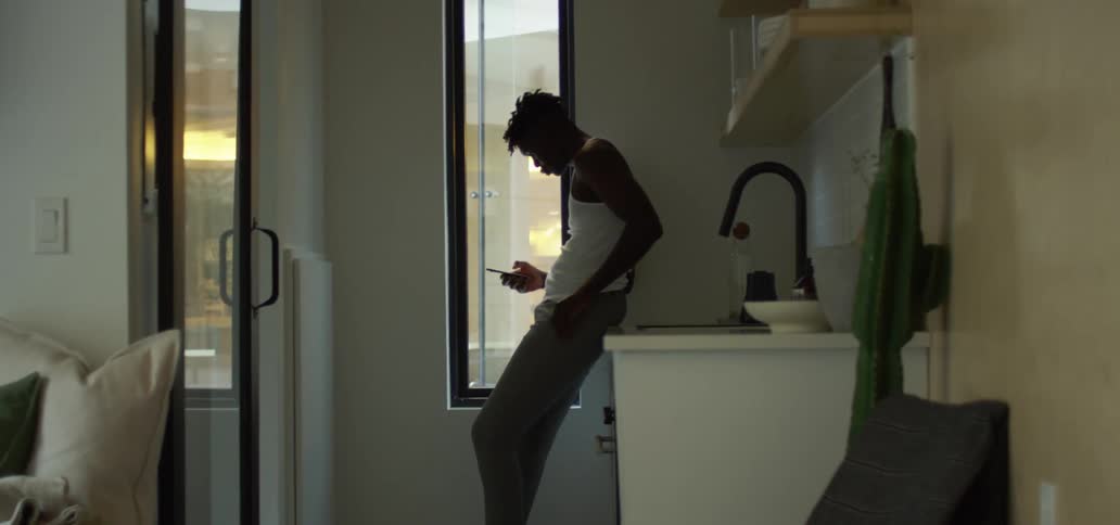 A black man leaning against a counter while using his smartphone