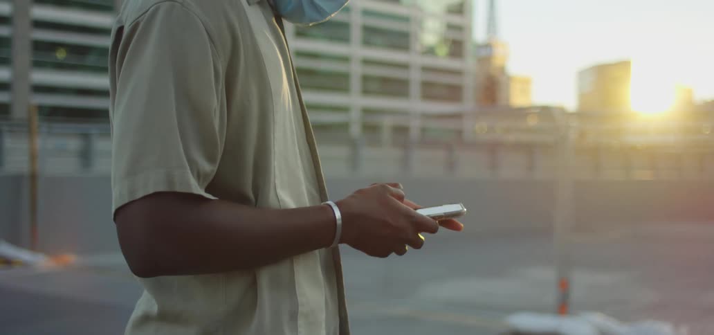 A teen in a face mask stands on a rooftop and uses his cell phone