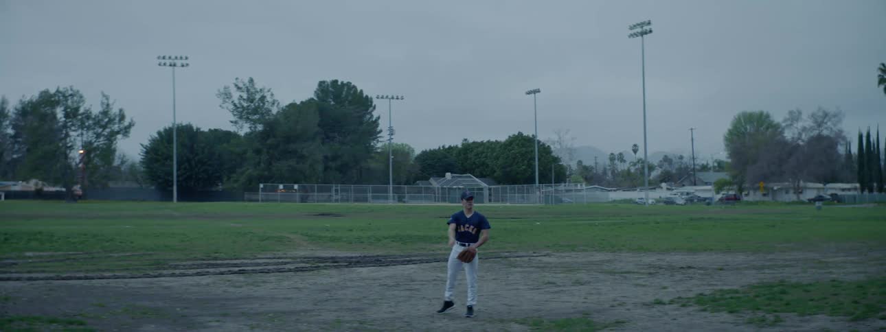 Baseball player wearing uniform stands in a field and throws a ball out of frame