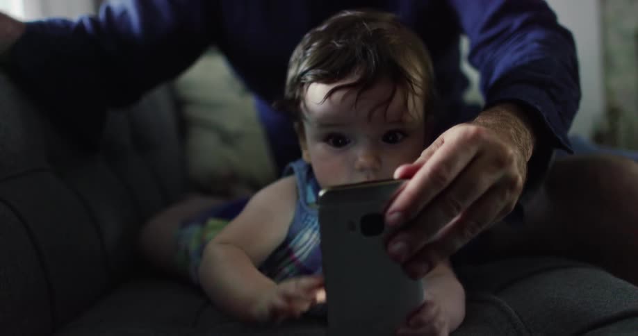 Man holds mobile phone for child to play with while sitting on couch