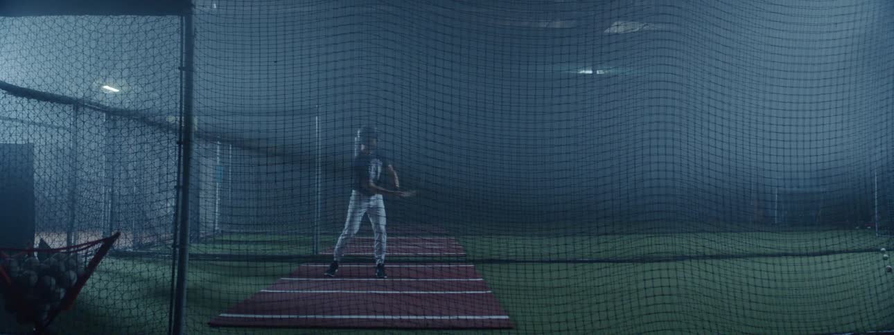 A baseball player practices at the batting cages hitting a ball at night