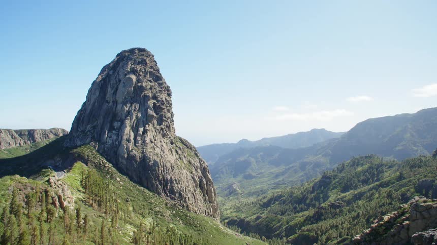 A bus drives down a road next to a steep mountain and a valley
