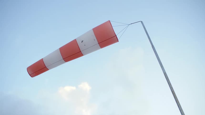 A long pole holds an orange and white windsock blowing in the wind