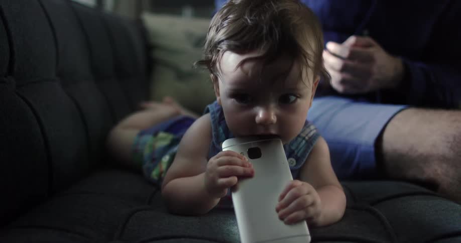 Baby gnawing on a cell phone while laying on a couch