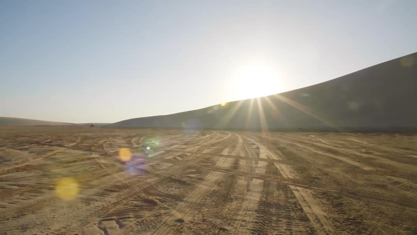 The sun shining over a large sand dune onto a barren plain covered in tire tracks