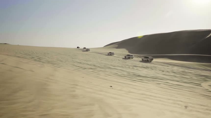 Convoy of suvs driving up a sand dune in the desert