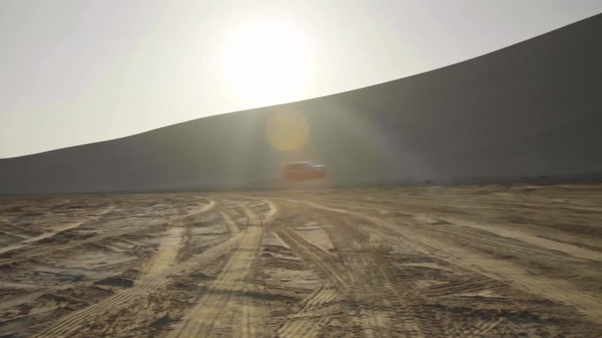 A vehicle drives up a sandy hill in a desert