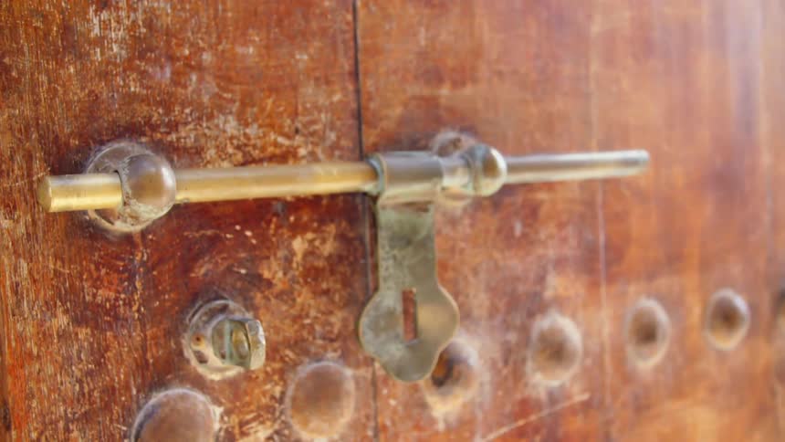 Metal door closure hangs above bolts on distressed wooden door