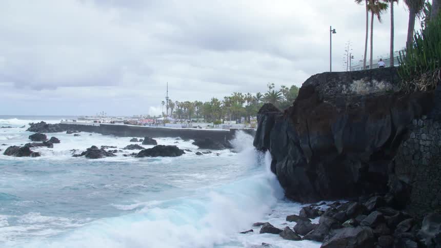 Ocean waves break against the rocky shore on a cloudy day