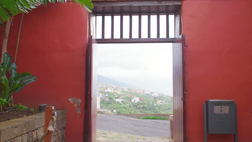 A white car drives by an entrance with open wooden doors