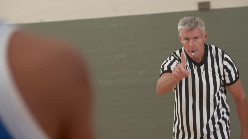 A referee blows his whistle and throws a basketball to a teen