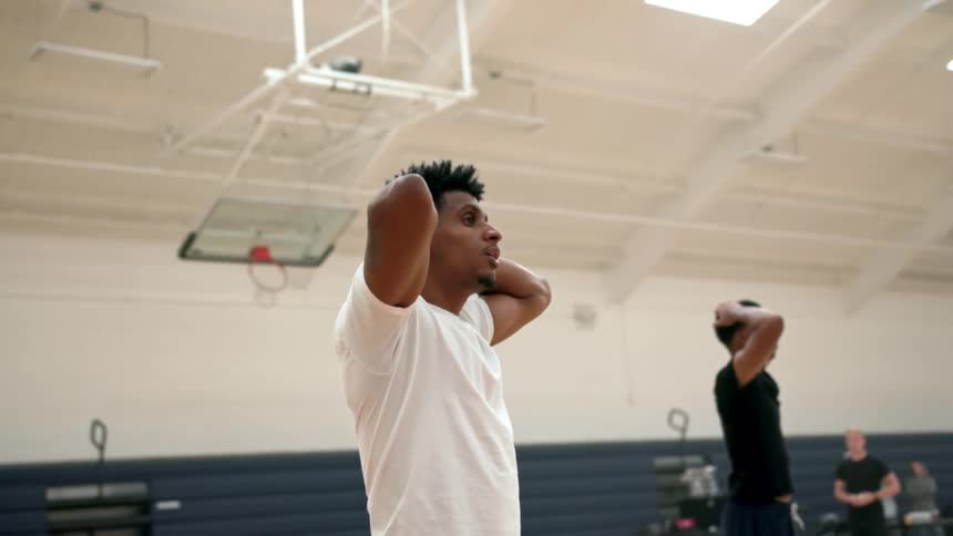 Two teenagers stand in a gym with their hands clasped behind their heads