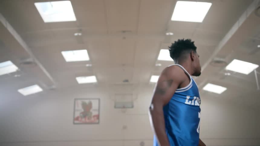 Black basketball player with blue jersey shoots a basketball through the hoop and raises an arm after scoring in the basketball court