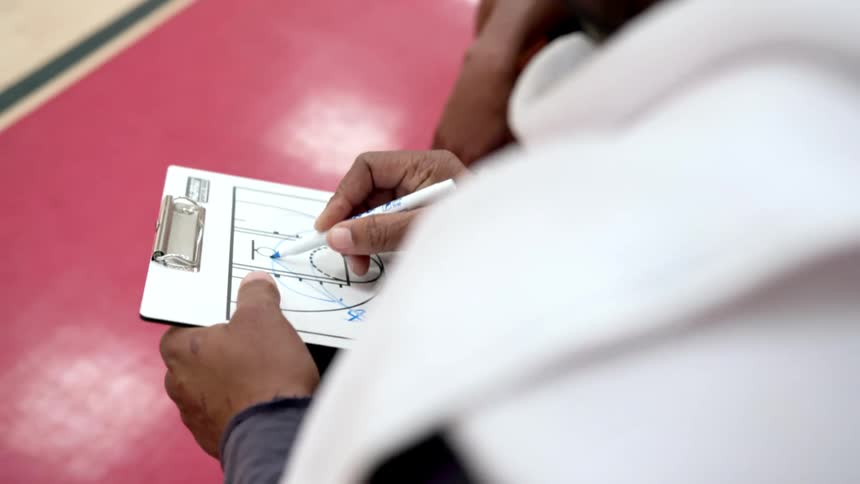 A basketball coach goes over plays by drawing on a white clipboard